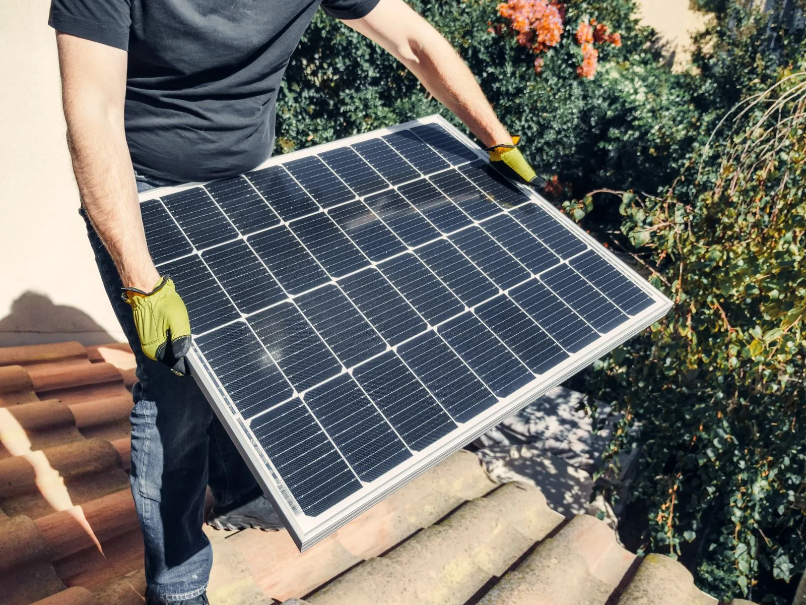 Instalator care transportă un panou fotovoltaic pe un acoperiș din țiglă